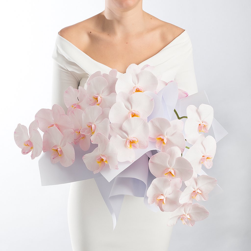 A woman earing black, holding a bouquet of soft pink phalaenopsis orchids in a bouquet.