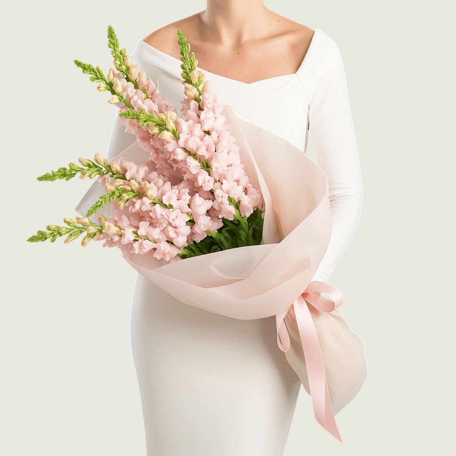 A woman wearing black holding a bouquet ot soft pink snapdragon flowers in a bouquet.